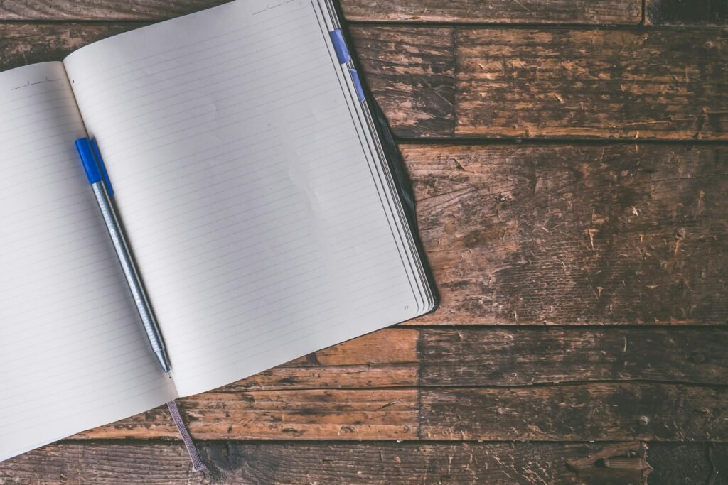 An open notebook with a blue pen lies on a rustic wooden table, inviting creativity and writing.