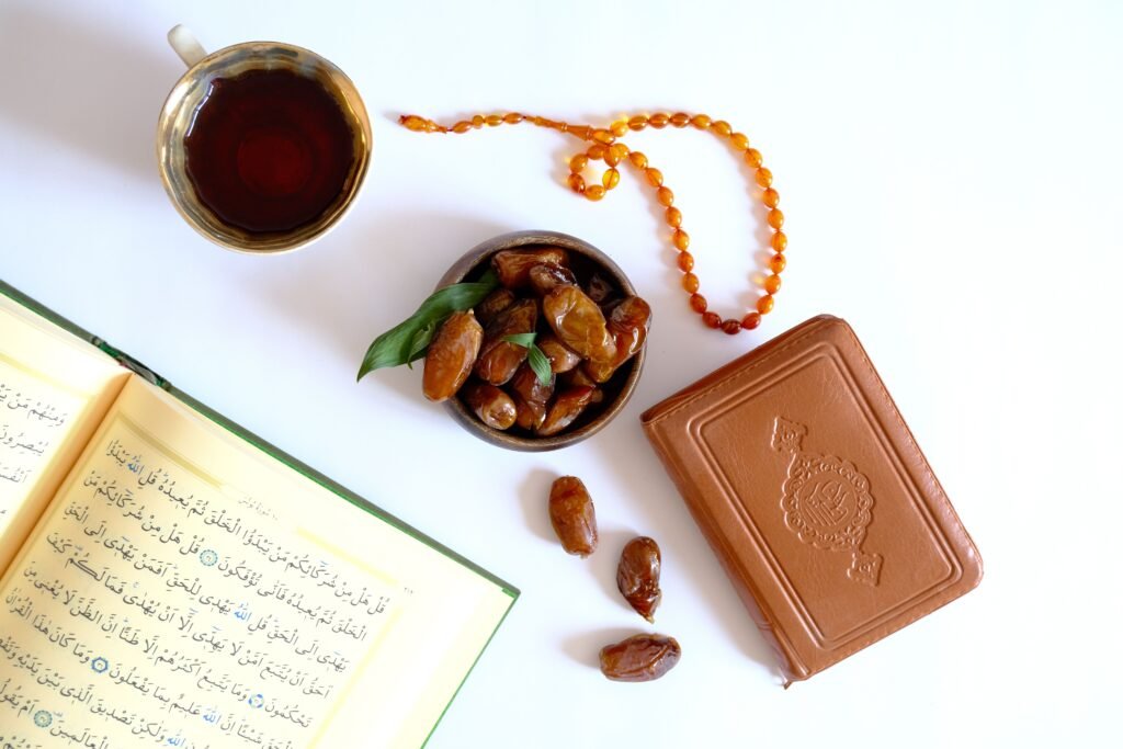 Flat lay of Quran, tea, dates, and prayer beads on white background.