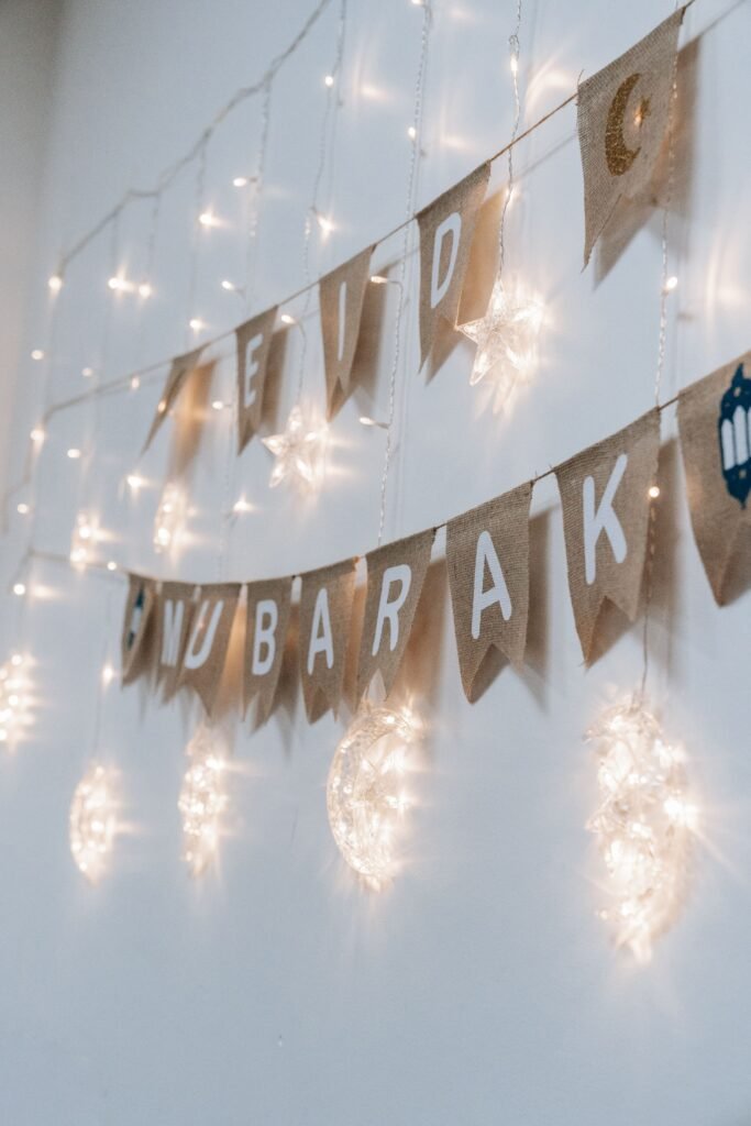 Festive Eid Mubarak banner with glowing string lights on a white wall.